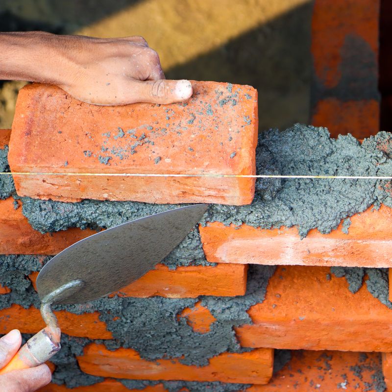 Maçon posant des briques au mortier avec une truelle – Blue Vert